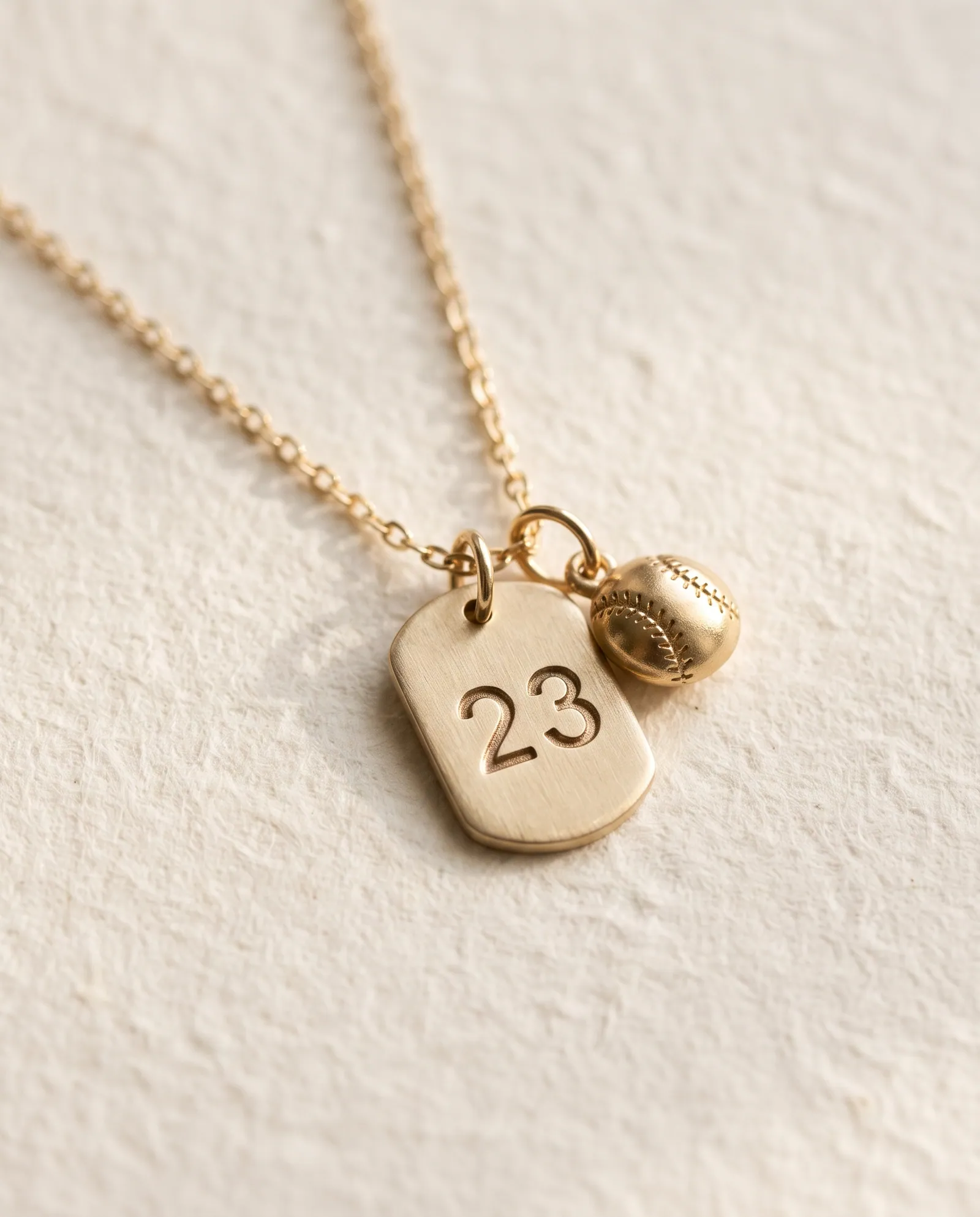 Gold-tone tag pendant stamped with the number 23 beside a small baseball charm