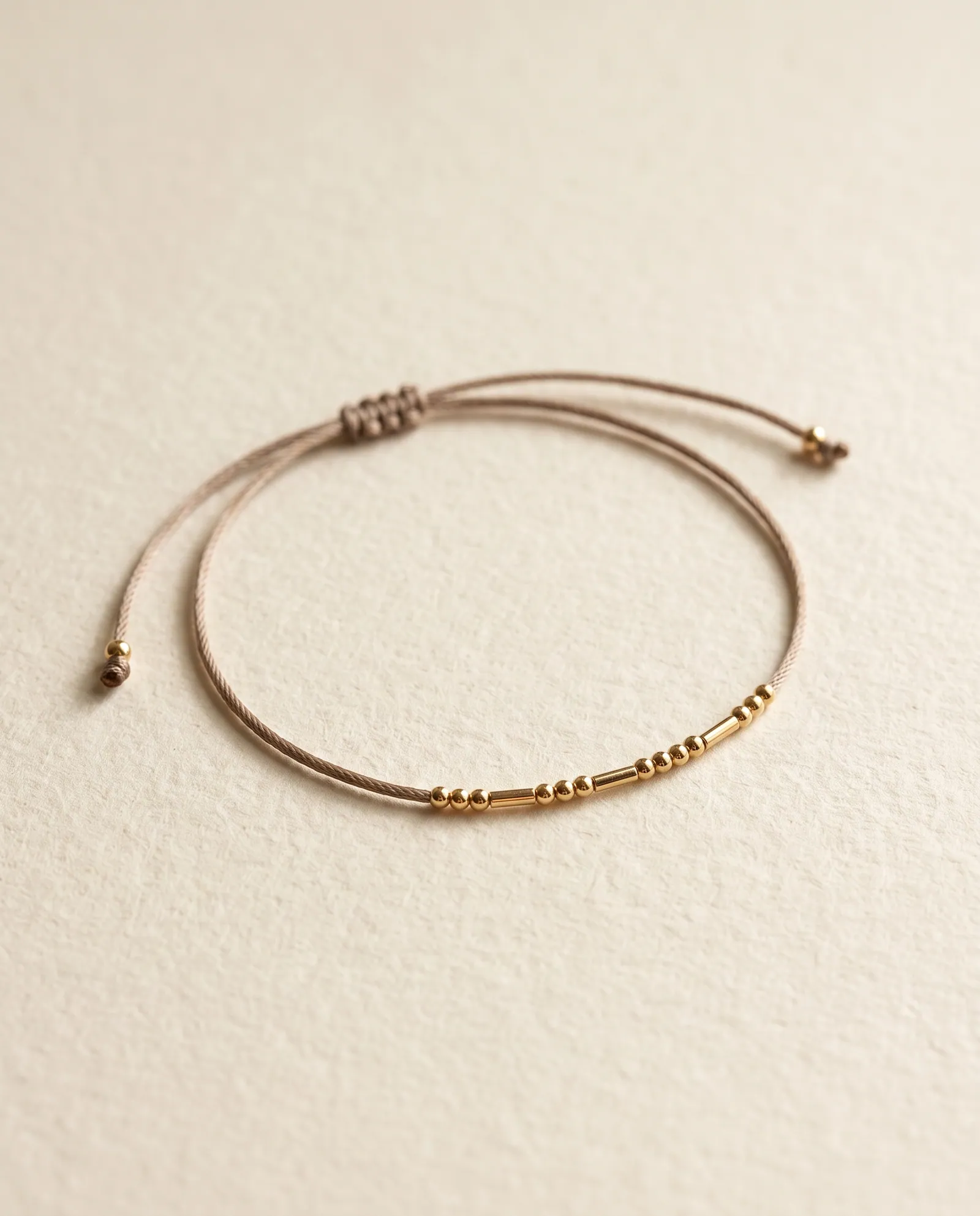 Taupe cord bracelet with gold-tone round and tube beads spelling a word in Morse code