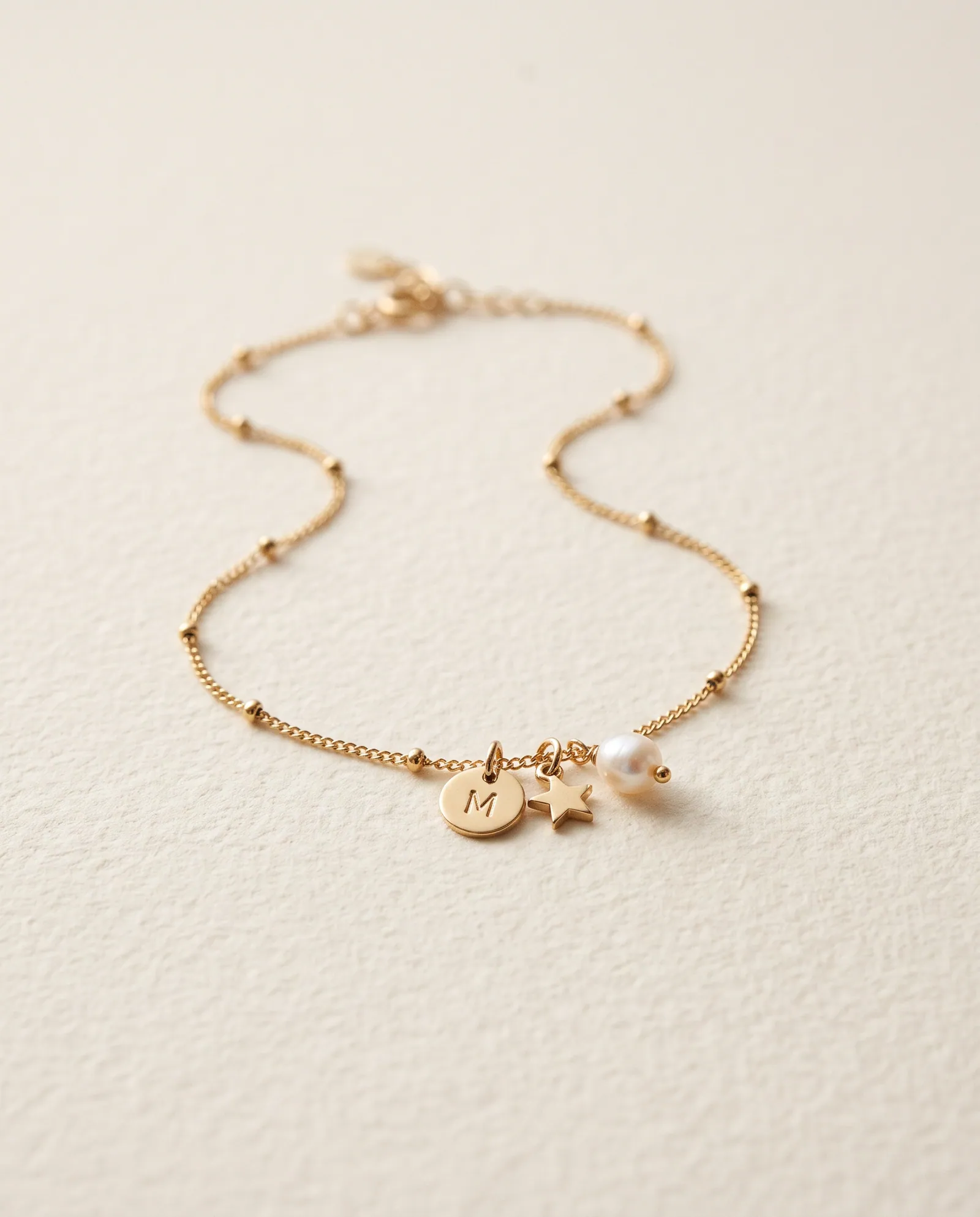 Fine gold-tone anklet with an initial M disc, star charm and small pearl