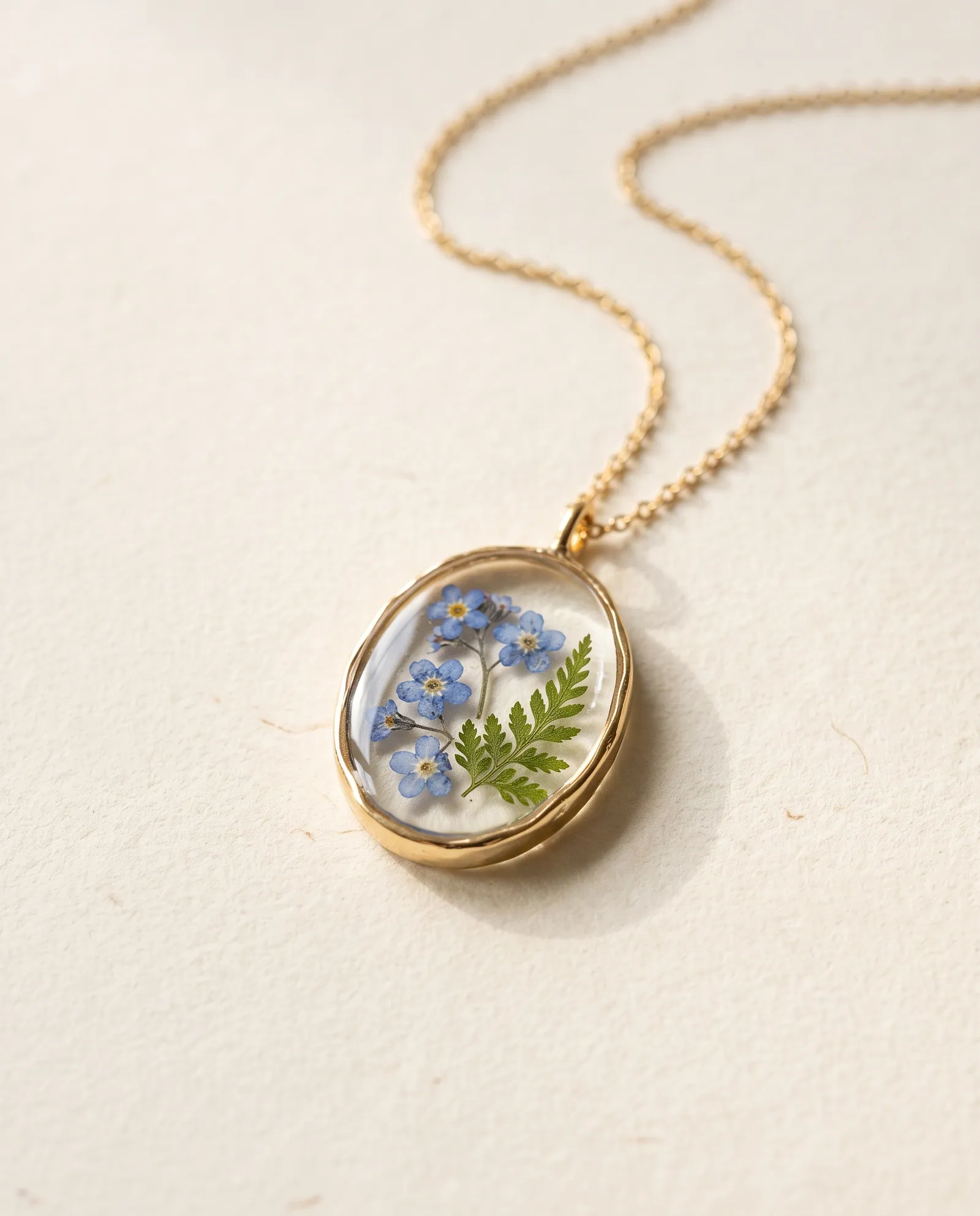 Oval clear resin pendant with pressed blue forget-me-not flowers in a gold-tone bezel