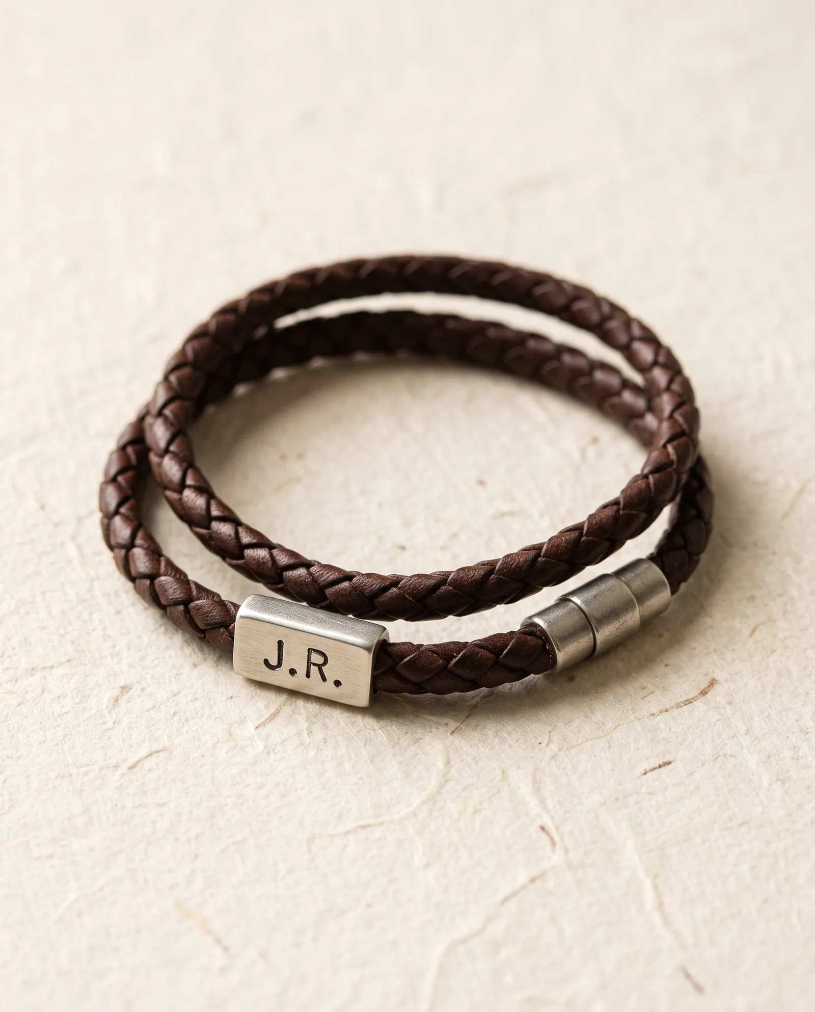 Braided brown leather bracelet with a silver-tone tag stamped J.R.
