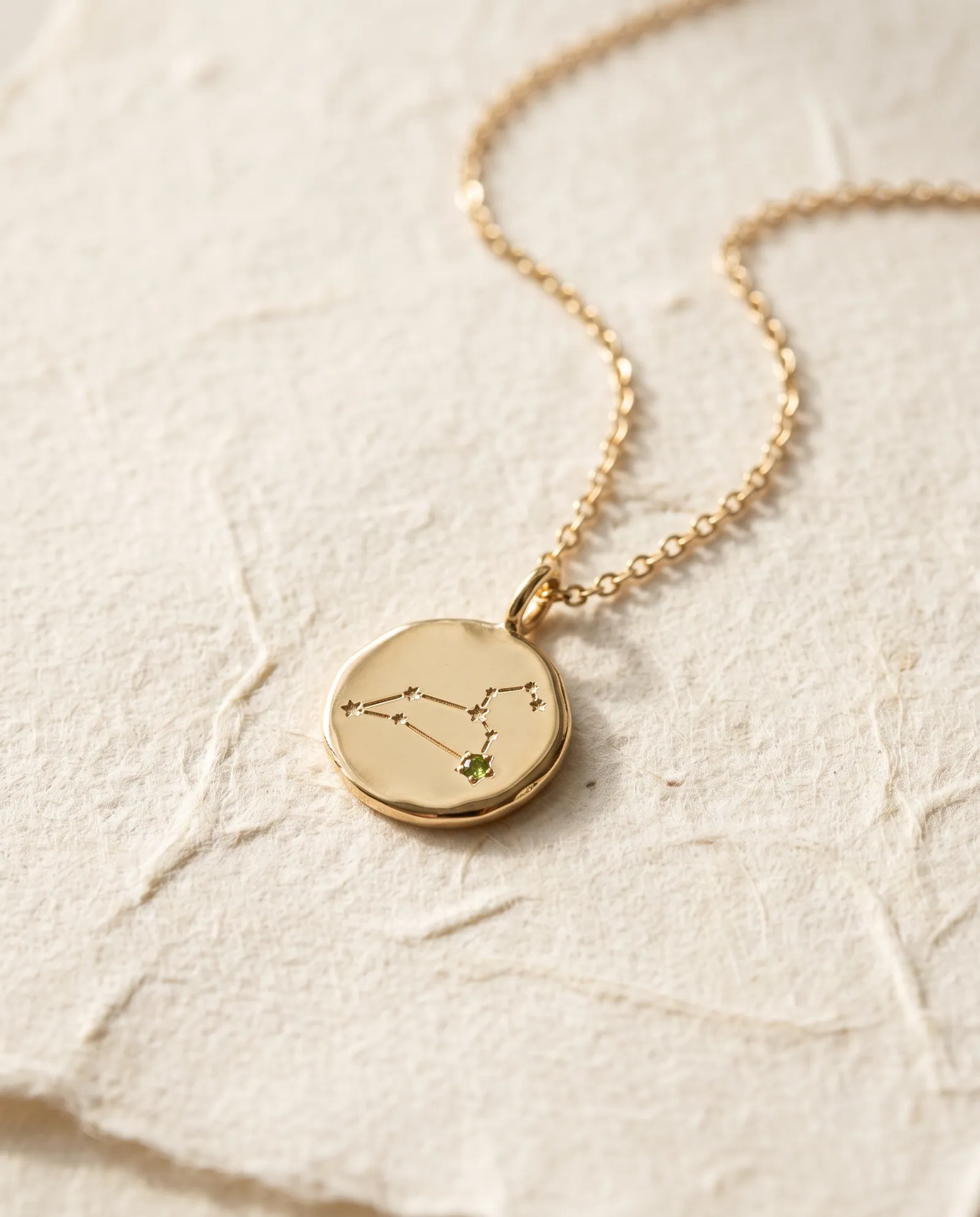 Small gold-tone coin pendant engraved with the Leo constellation and a tiny peridot-colored stone